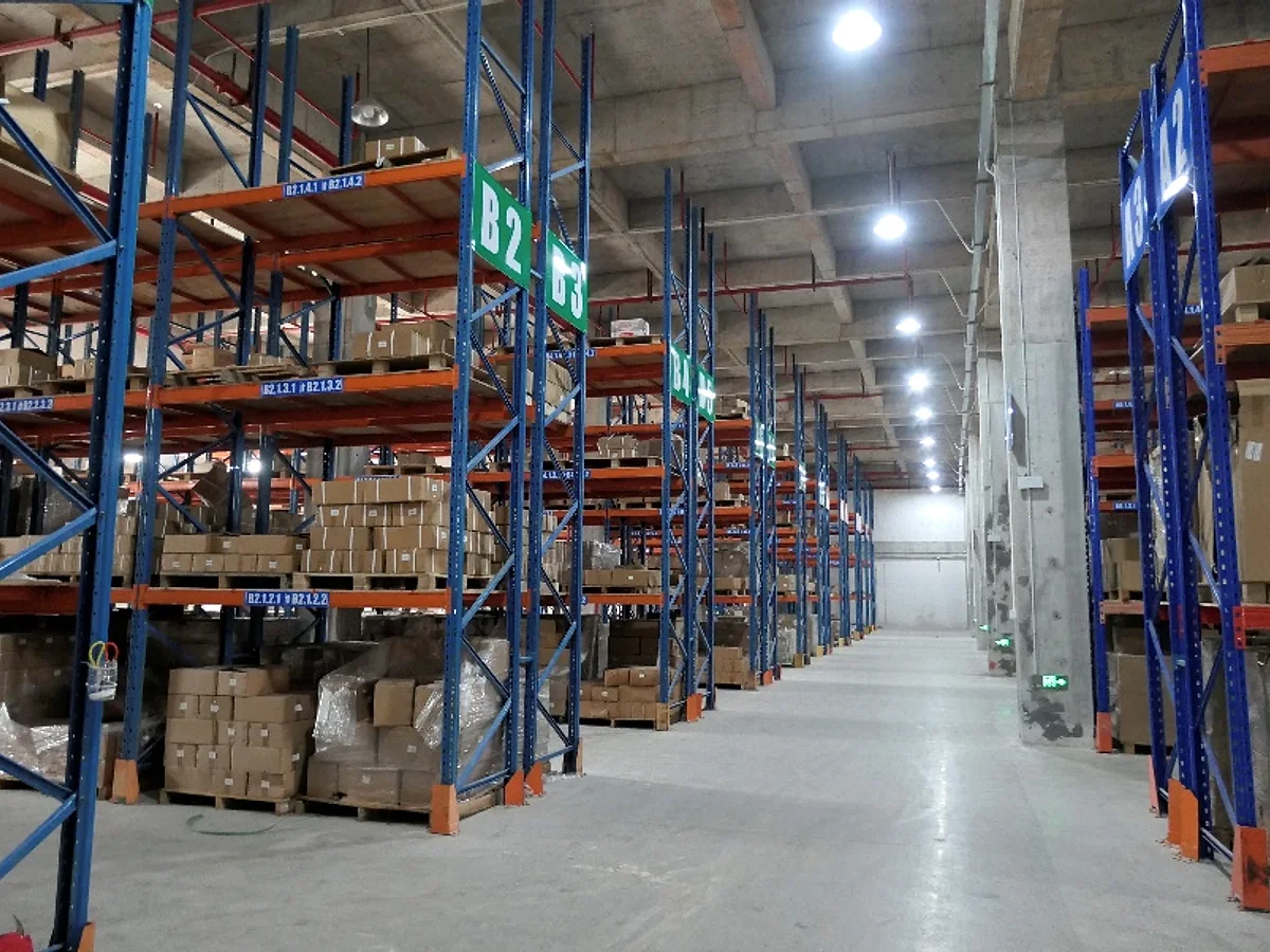 Entrepôt avec rayonnages bleus et orange contenant des pièces moteur en carton